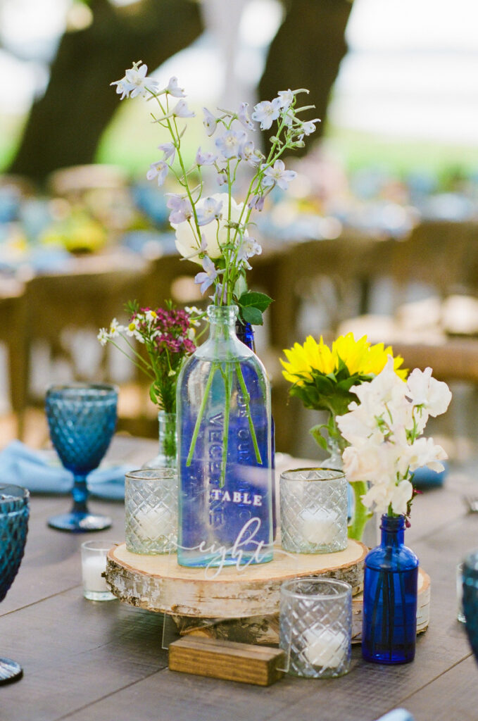 Lowndes Grove wedding bespoke reception decor with wood rounds and vintage bottles with summer flowers