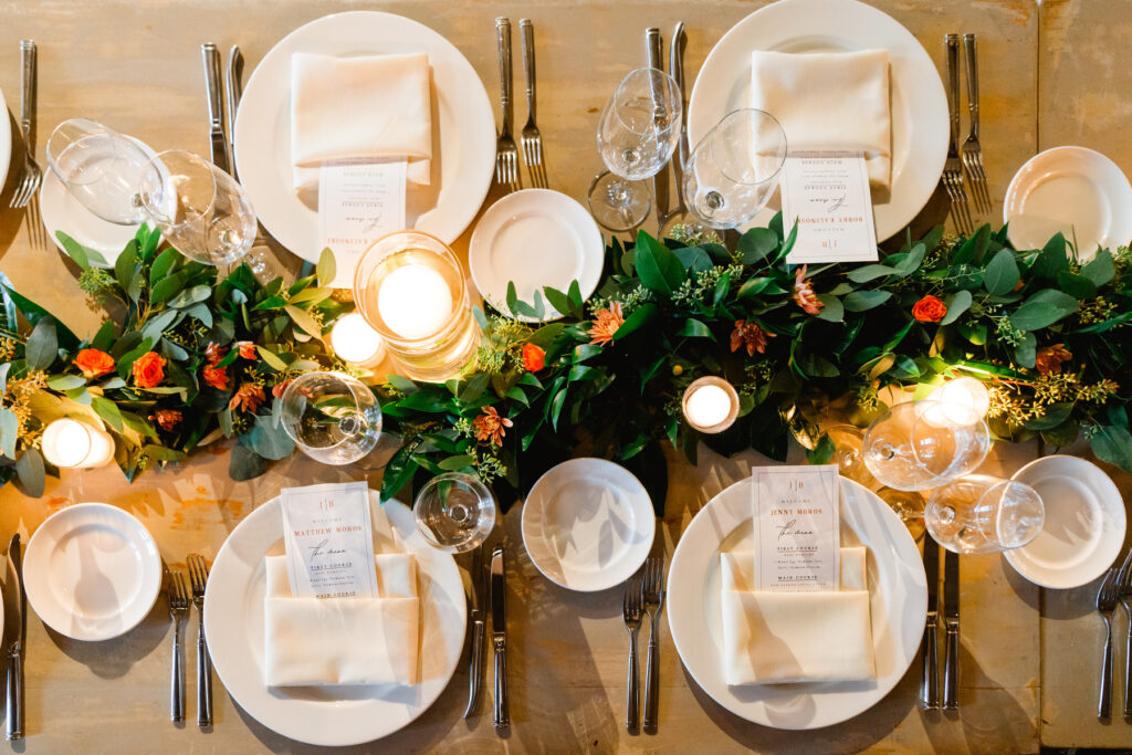 Overhead photo of place setting with white places, silver cutlery, and cascading greenery with pink and orange flowers and floating candles at a Cannon Green Wedding