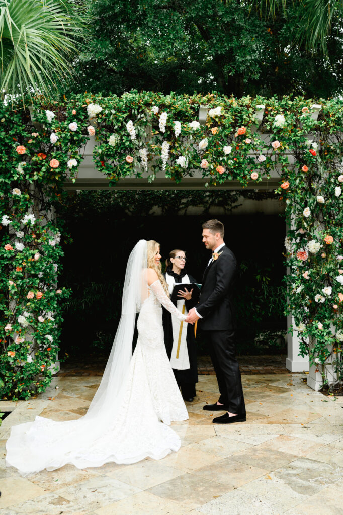 Bride and groom standing under the floral arbor during the ceremony at a Cannon Green Wedding