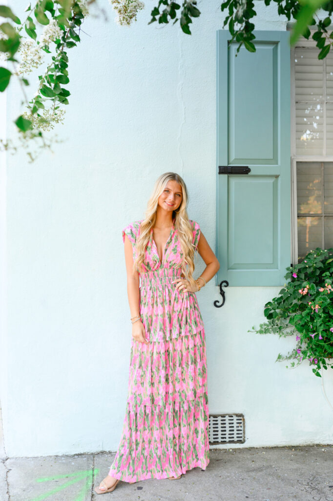 Young woman in pink and green maxi dress in front of blue historic house on Rainbow Row in Charleston, SC