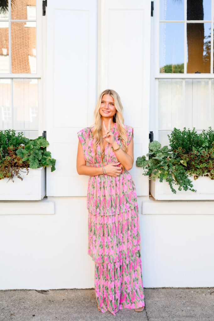 Young woman in pink and green maxi dress in front of white historic house on Rainbow Row in Charleston, SC