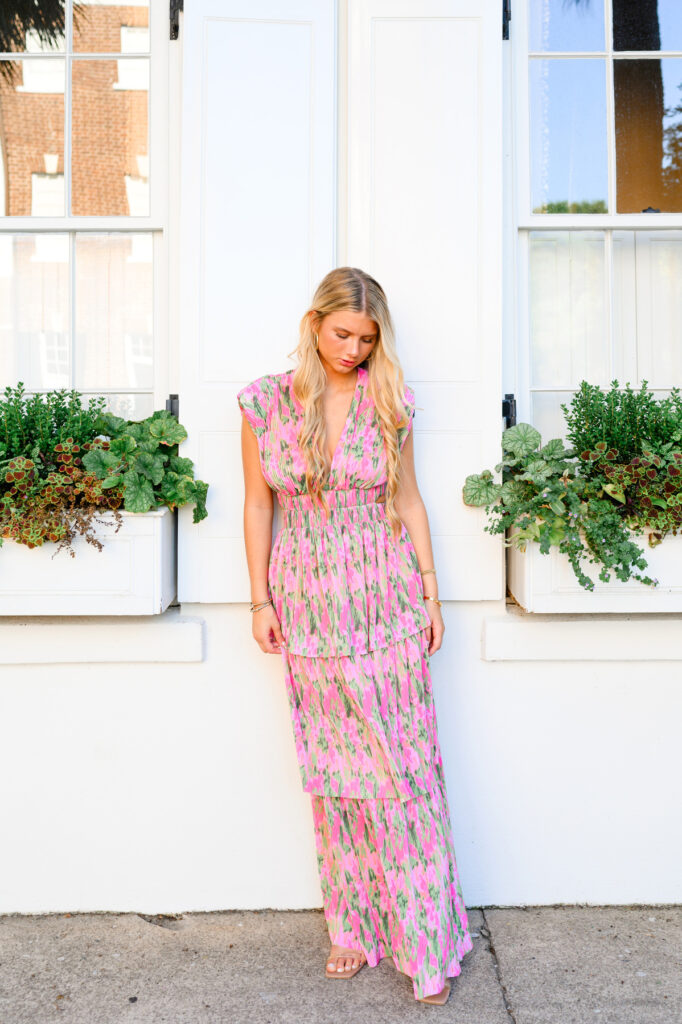 Young woman in pink and green maxi dress in front of white historic house on Rainbow Row in Charleston, SC