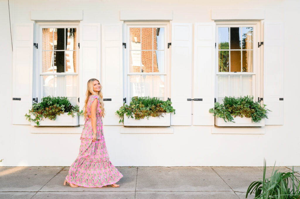 Young woman in pink and green maxi dress in front of white historic house on Rainbow Row in Charleston, SC