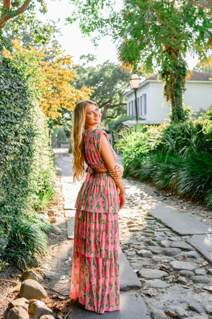 Young woman in pink and green maxi dress in a cobblestone ally downtown Charleston, SC