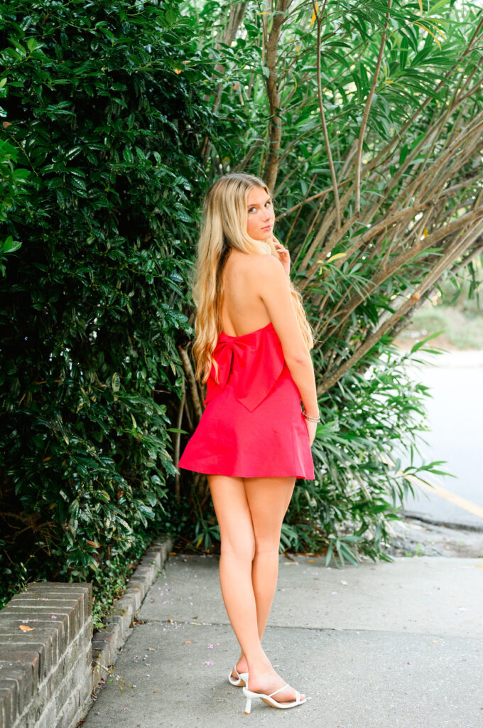 A young woman with blond hair wearing a strapless red dress with a bow in the back in historic downtown Charleston, SC, on S Adgers Wharf