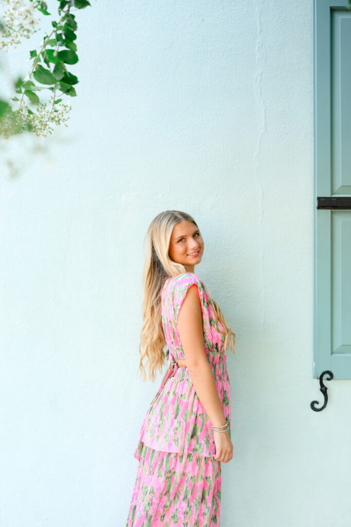 Young woman in pink and green maxi dress in front of blue historic house on Rainbow Row in Charleston, SC