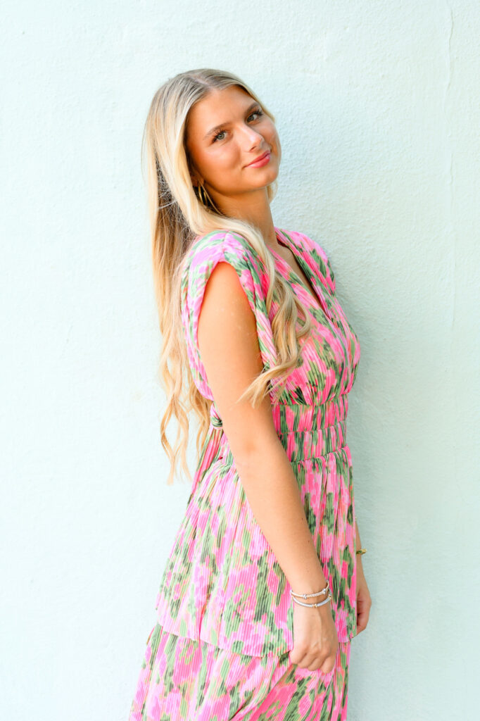 Young woman in pink and green maxi dress in front of blue historic house on Rainbow Row in Charleston, SC