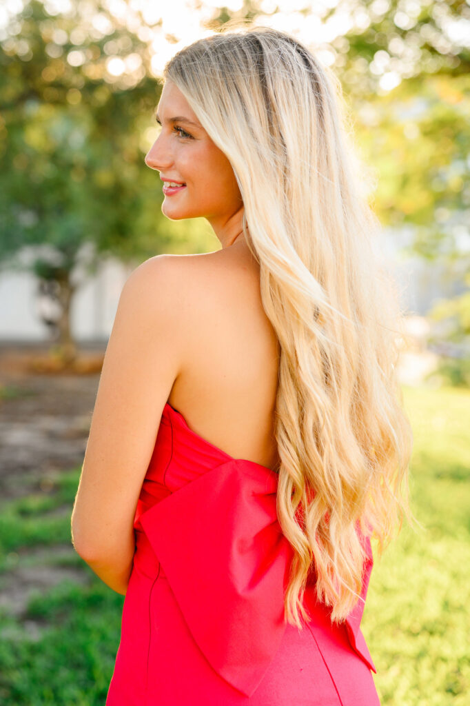 A young woman with blond hair wearing a strapless red dress with a bow in the back in historic downtown Charleston, SC, at Waterfront Park