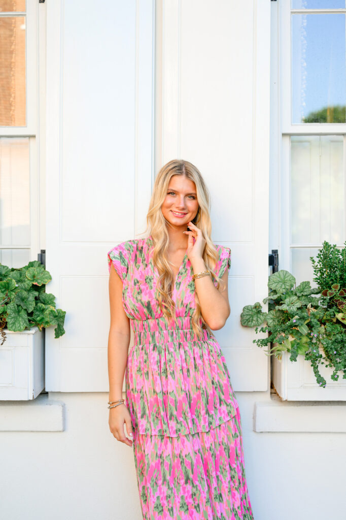 Young woman in pink and green maxi dress in front of white historic house on Rainbow Row in Charleston, SC