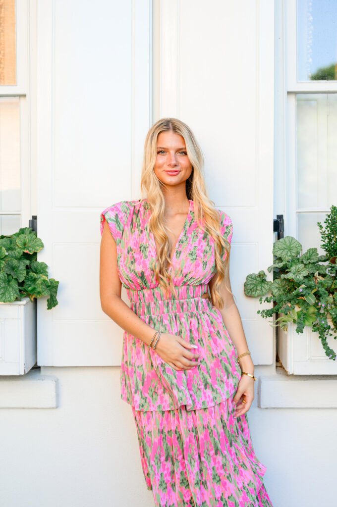 Young woman in pink and green maxi dress in front of white historic house on Rainbow Row in Charleston, SC