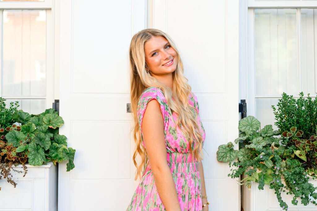 Young woman in pink and green maxi dress in front of white historic house on Rainbow Row in Charleston, SC