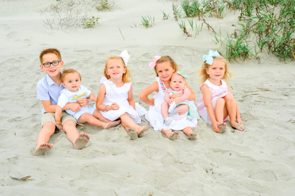 Grandchildren sit together on the sand during a Kiawah beach family photo