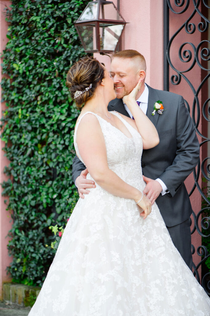 Cedar Room wedding portrait of bride and groom in front of pink house on Rainbow Row while nuzzling