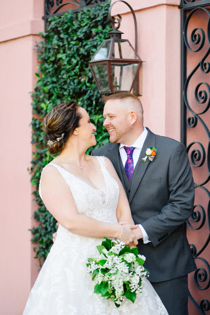 Cedar Room wedding portrait of bride and groom in front of pink house on Rainbow Row while looking at each other