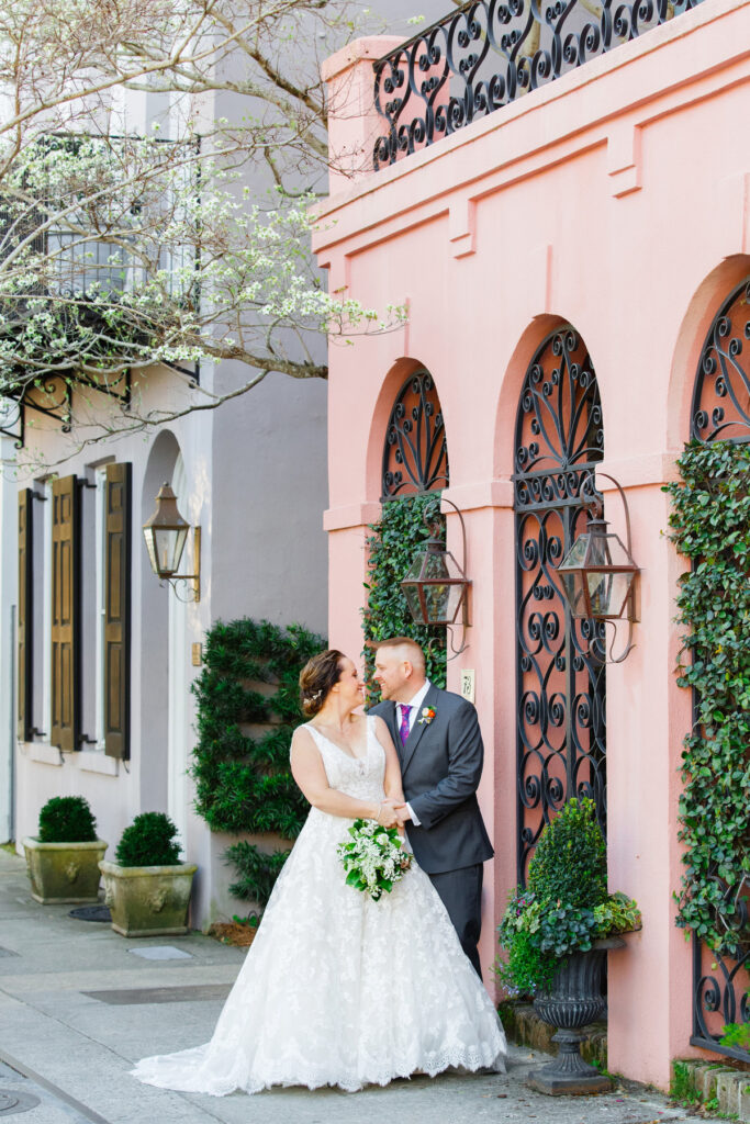 Cedar Room wedding portrait of bride and groom looking at each other in front of pink house on Rainbow Row