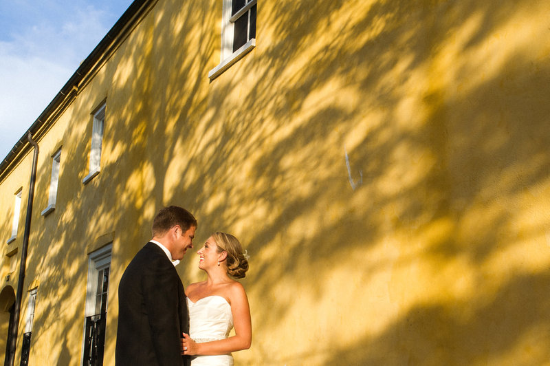 A groom in a black tux and a bride in a white dress pose for a portrait at the William Aiken House after their First Baptist Church wedding ceremony.