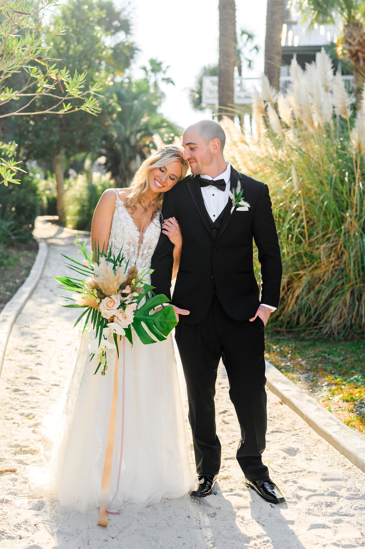 A bride and groom pose for a portrait during their Wild Dunes wedding day. Bride is in a sleeveless white dress. Groom is in a black tux.