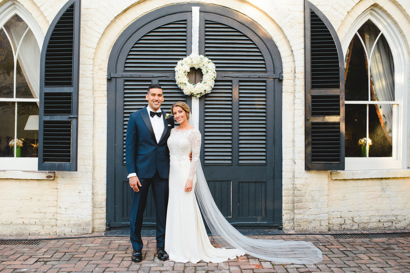 A groom in a blue tux and a bride in a long sleeve white dress pose for a portrait at their Winter William Aiken House wedding