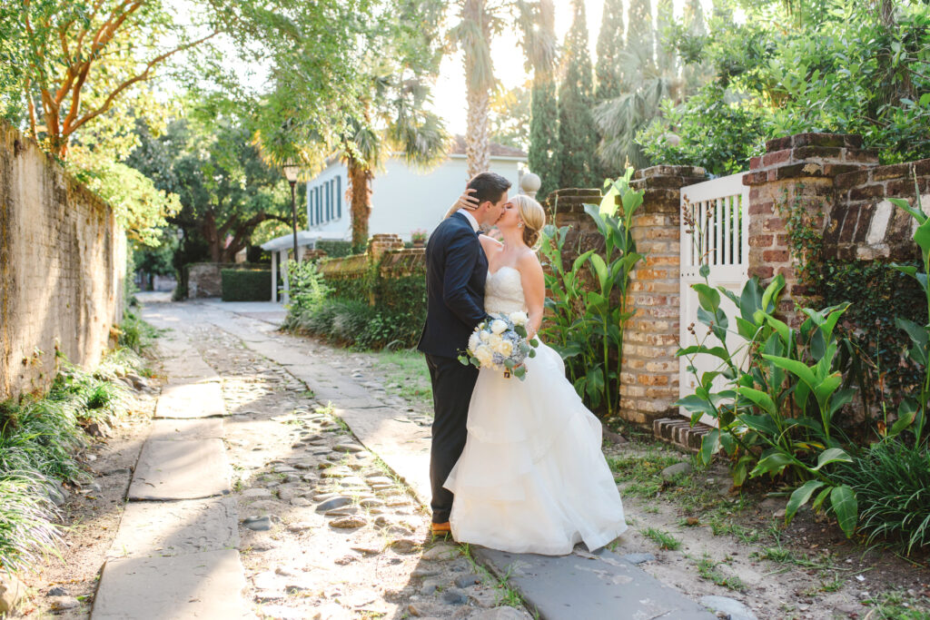 A bride and groom kiss in a cobblestone alleyway after their brunch William Aiken House wedding in Charleston, SC